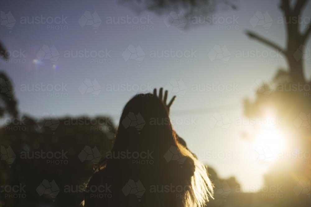 Girl from behind reaching out to setting sun - Australian Stock Image