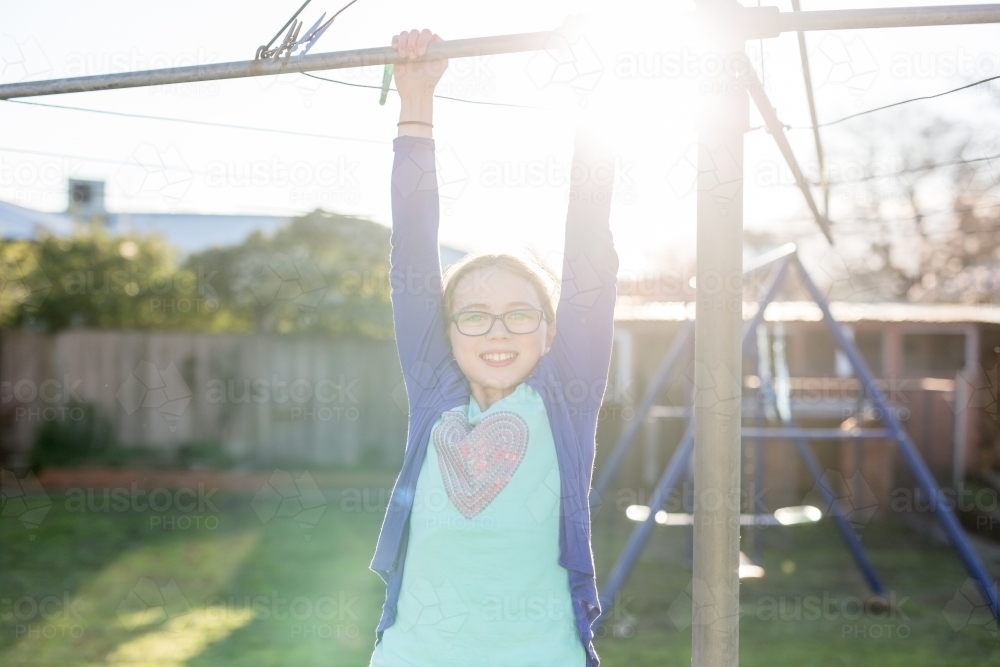 Girl hanging from washing line, backlit by sun - Australian Stock Image