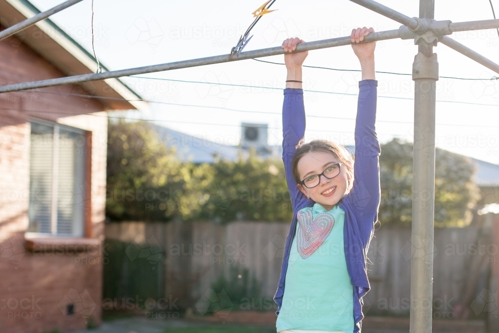 Girl hanging from washing line in backyard - Australian Stock Image