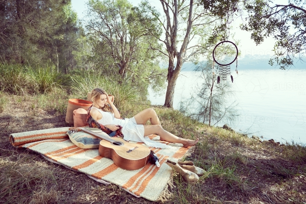Girl having a picnic by the river with a guitar - Australian Stock Image