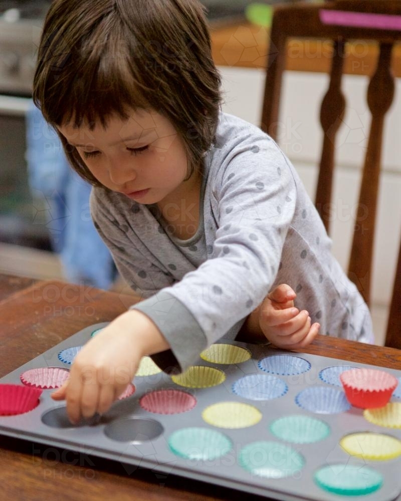 Girl helping bake cupcakes by putting patty pans in a baking tin - Australian Stock Image