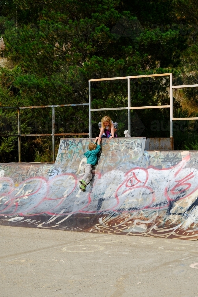 Girl helping boy up a skate park ramp - Australian Stock Image