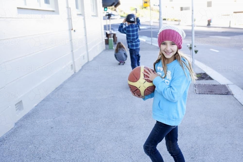 Girl holding basketball playing with siblings along a street - Australian Stock Image