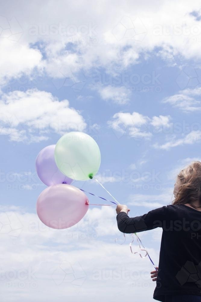 Girl holding bunch of balloons looking up at them - Australian Stock Image