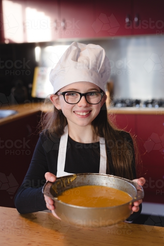 Girl holding cake tin with batter smiling at camera - Australian Stock Image