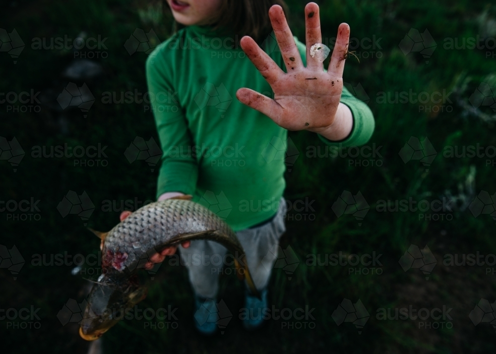 Girl holding carp showing dirty hand - Australian Stock Image