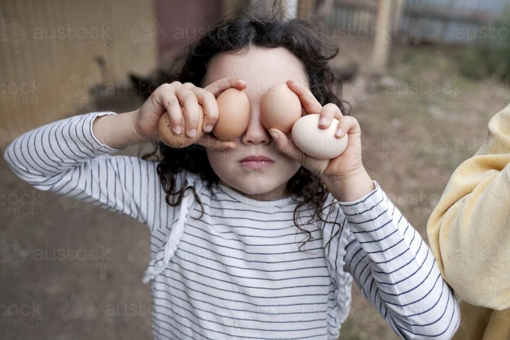 Girl holding freshly gathered free range eggs over her eyes - Australian Stock Image