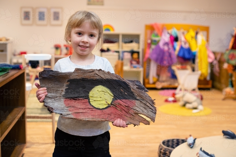 Girl holding painted Aboriginal flag on tree bark - Australian Stock Image