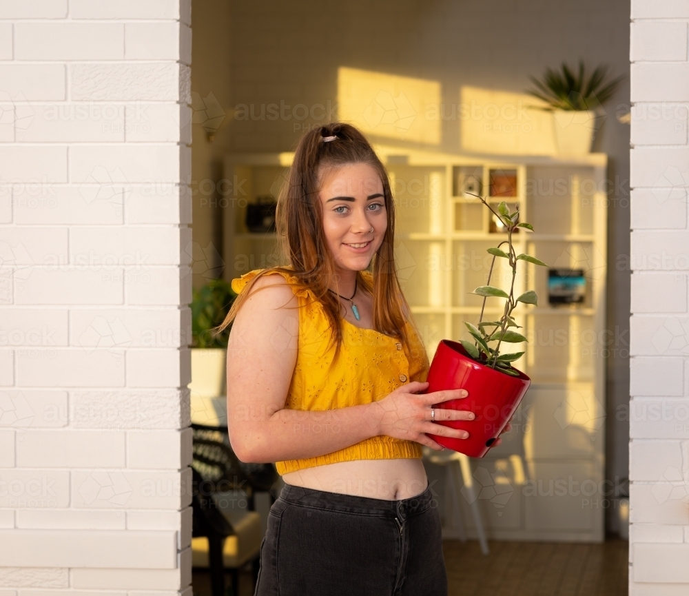 girl holding pot with plant in sunlit room - Australian Stock Image