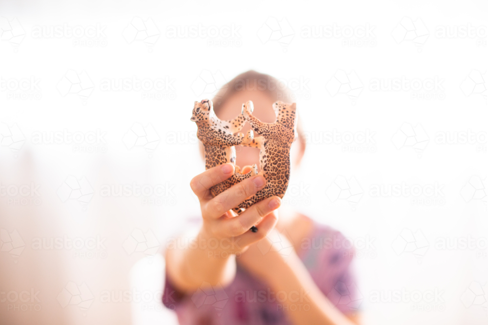 girl holding up plastic toy cheetahs during a game - Australian Stock Image