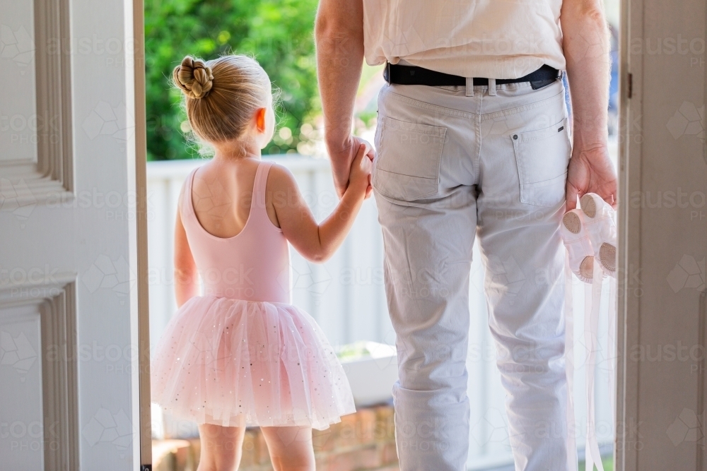 Girl in ballet leotard walking out door with dad holding her dance shoes on their way to lessons - Australian Stock Image