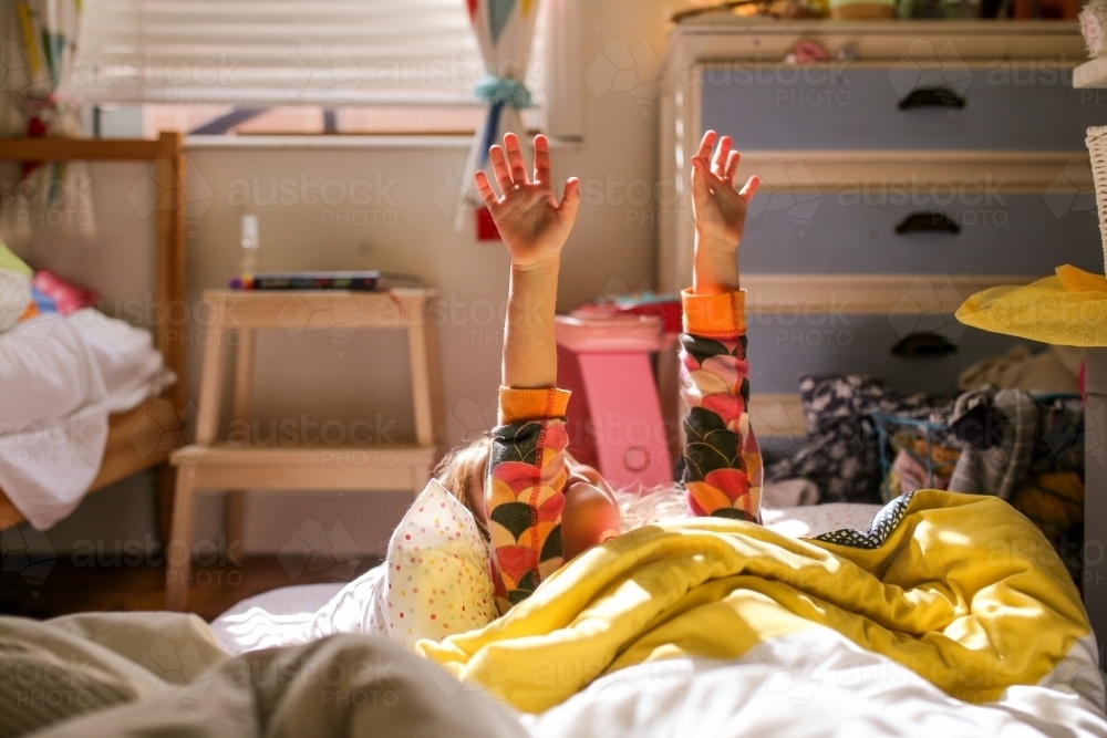Girl in bed waking up in morning sunlight putting her arms up - Australian Stock Image