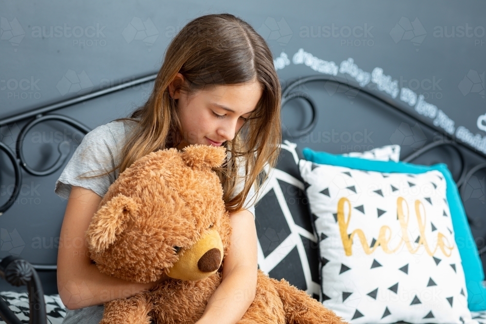 girl in bedroom cuddling teddy bear - Australian Stock Image