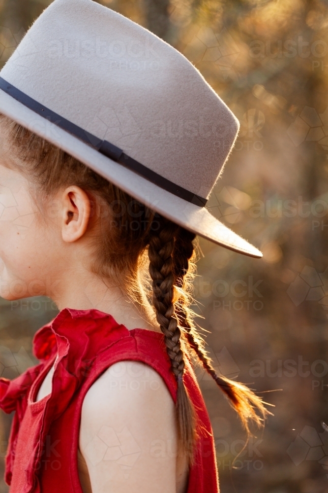 Girl in country style hat with plaited brown hair braids on farm - Australian Stock Image