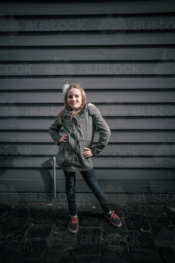 Girl in grey standing in front of grey weatherboards in the city - Australian Stock Image
