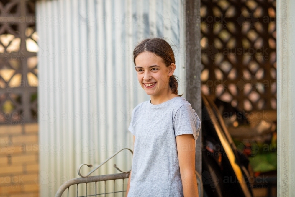 girl in grey t-shirt entering yard from shed - Australian Stock Image