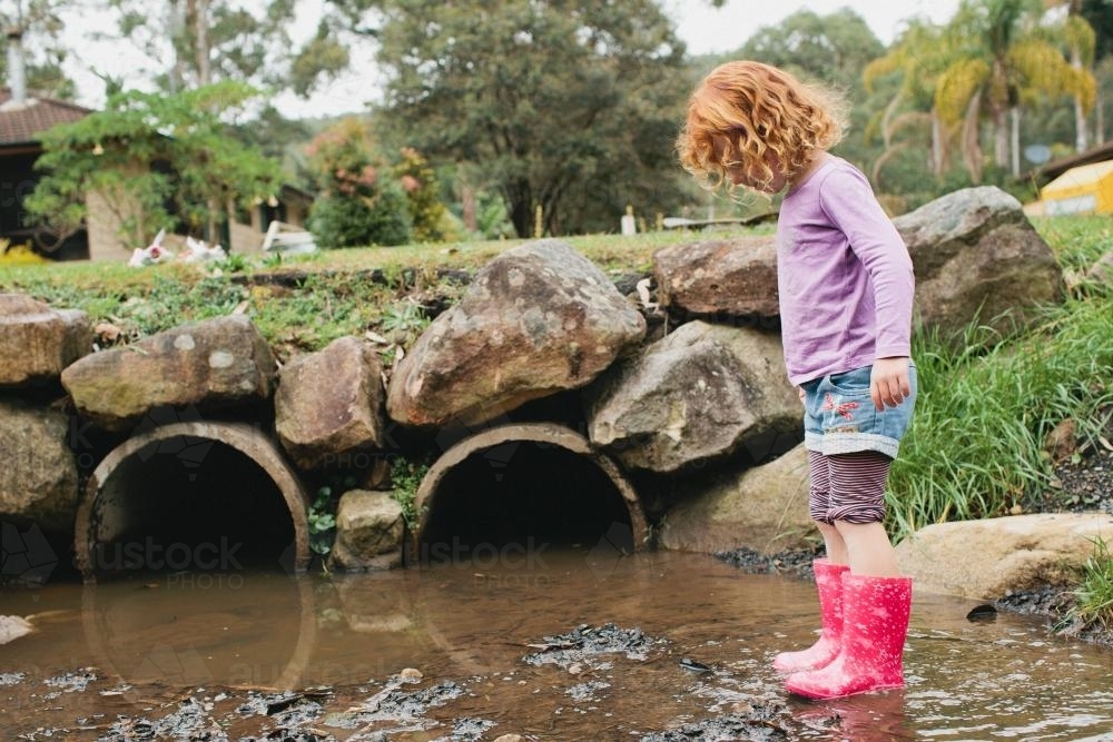 Girl in gumboots playing in a drain - Australian Stock Image