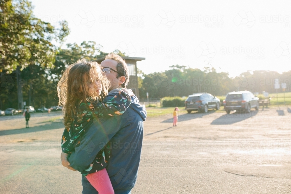 Girl in her father's arms, cranky to be leaving - Australian Stock Image