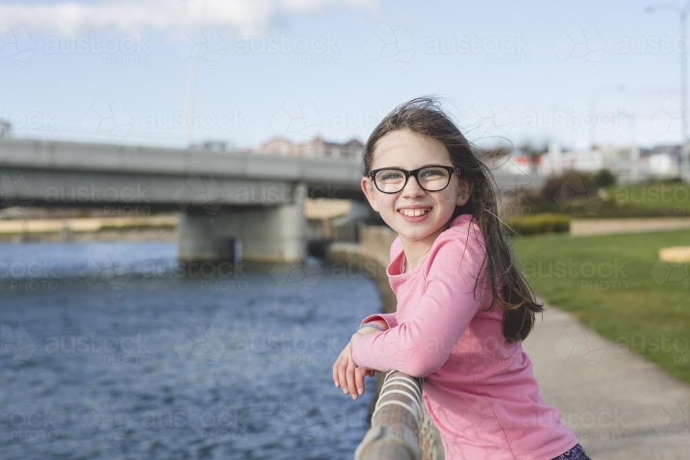 Girl in pink top standing at waters edge, smiling - Australian Stock Image