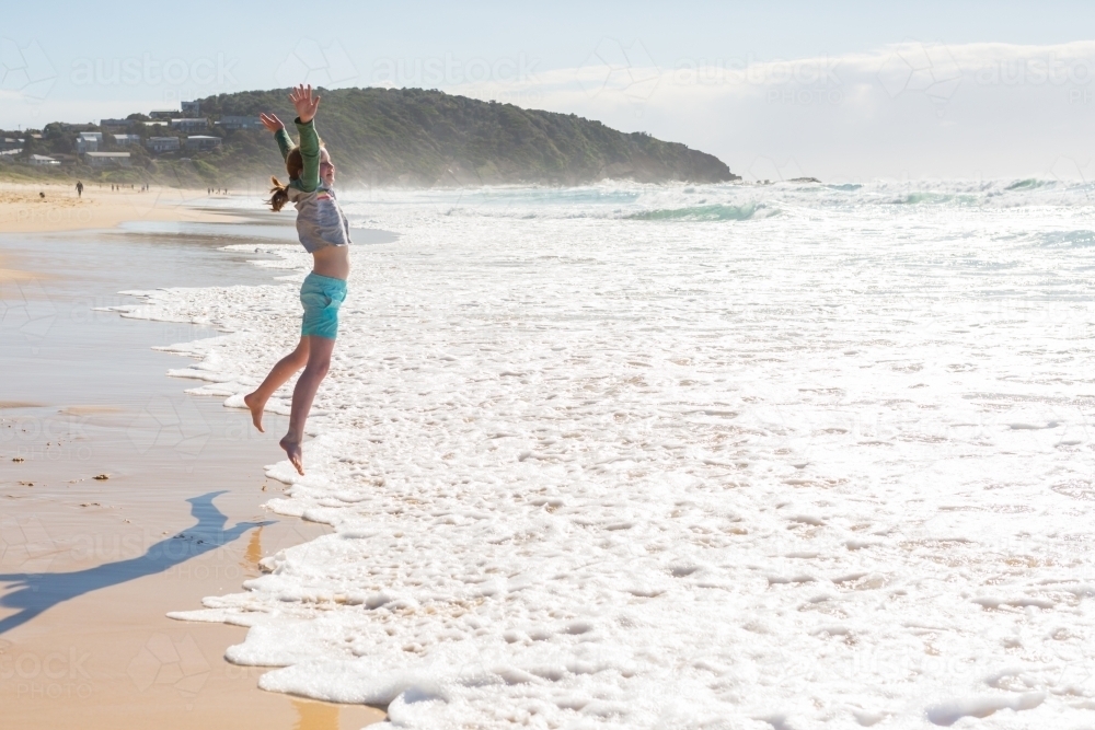Girl jumping at a beach looking out to sea - Australian Stock Image