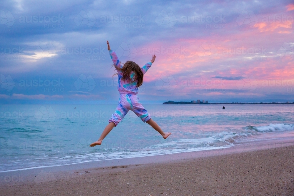 girl jumping in a tracksuit at the beach at dusk - Australian Stock Image