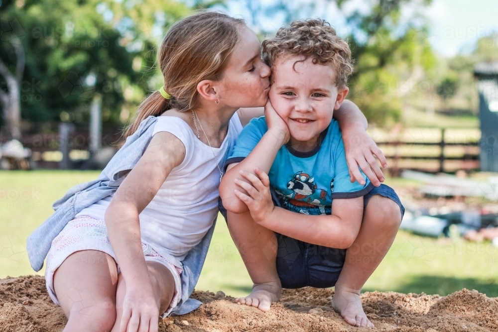 Girl kissing boy on forehead sitting on pile of dirt - Australian Stock Image
