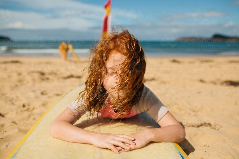 Girl laying on a surfboard at the beach - Australian Stock Image