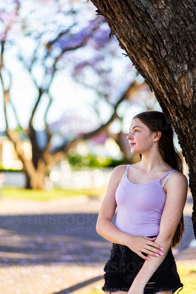 Image of Girl leaning against a tree looking away thinking - Austockphoto