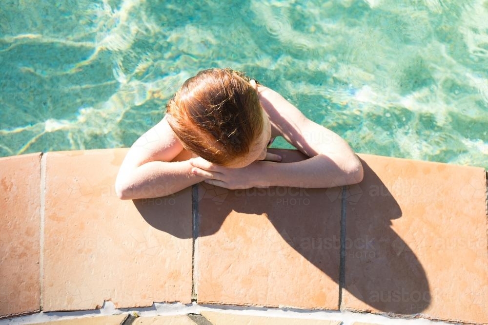 Girl leaning on the side of a swimming pool - Australian Stock Image