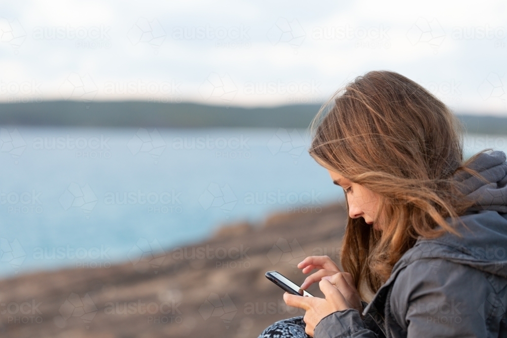 Girl looking at smartphone near the sea - Australian Stock Image