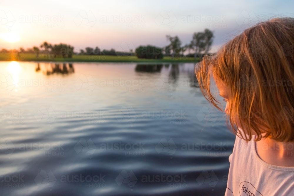 Girl looking at water on a boat cruise on yellow waters at sunset - Australian Stock Image