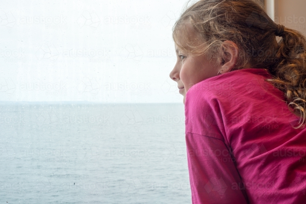 Girl looking out ship window to the ocean - Australian Stock Image