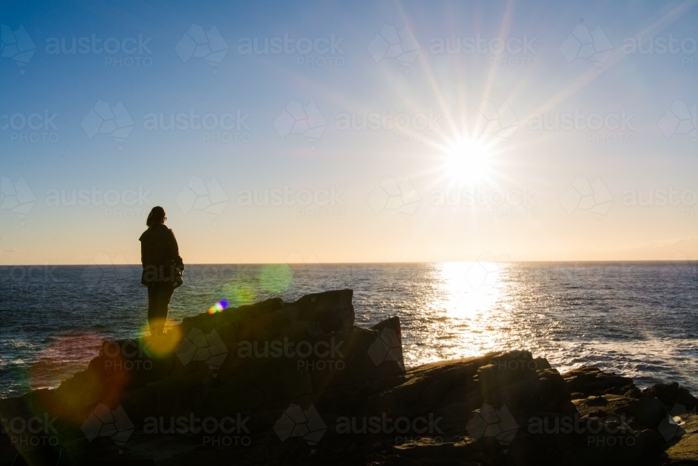 Girl looking out to sea during sunrise from a cliffside - Australian Stock Image