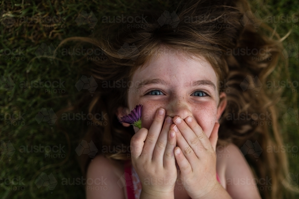 Girl lying on grass outside with flowers - Australian Stock Image