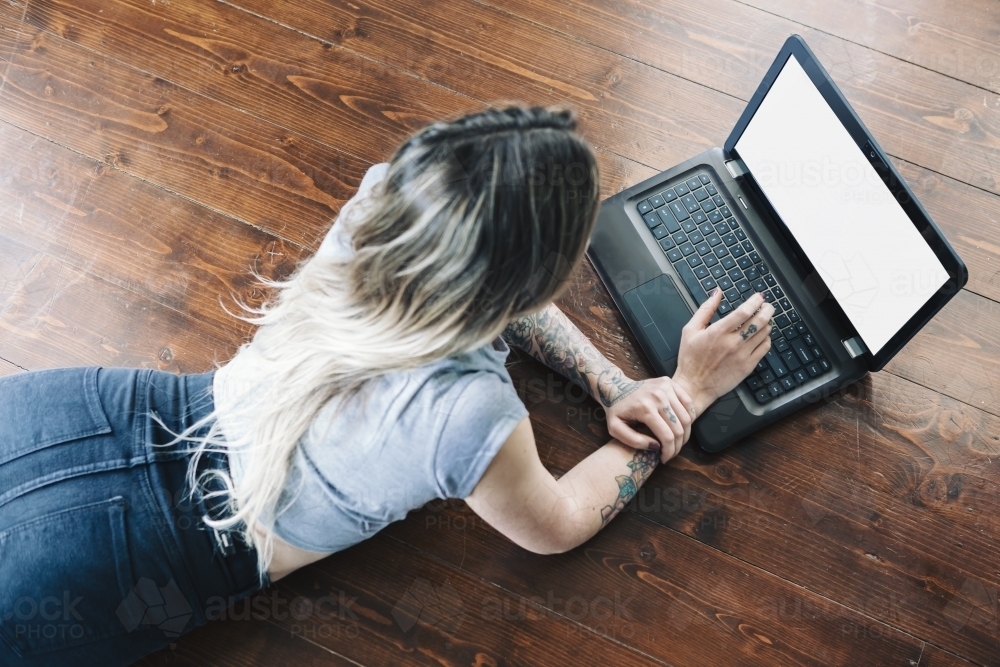 Girl lying on the floor working or studying using a laptop computer - Australian Stock Image