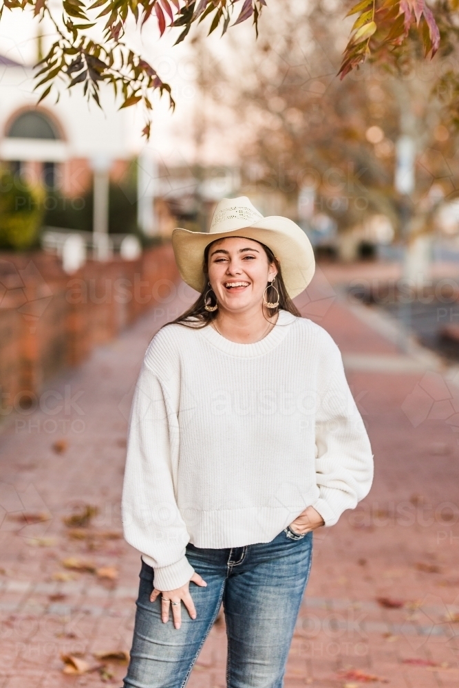 Girl on street laughing with hand in pocket wearing hat - Australian Stock Image