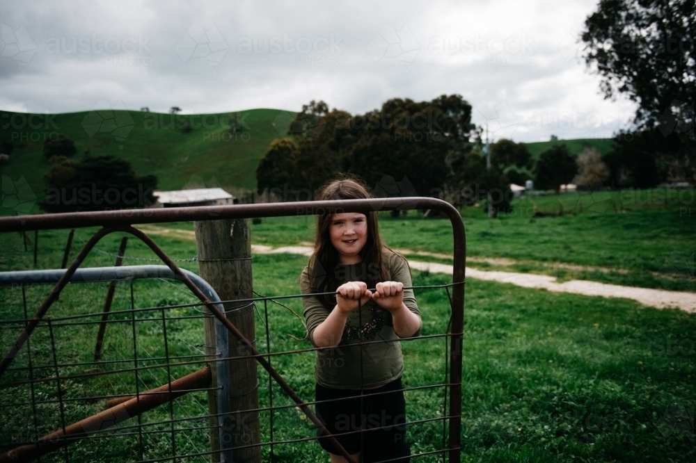 Girl opening a farm gate, looking at camera - Australian Stock Image