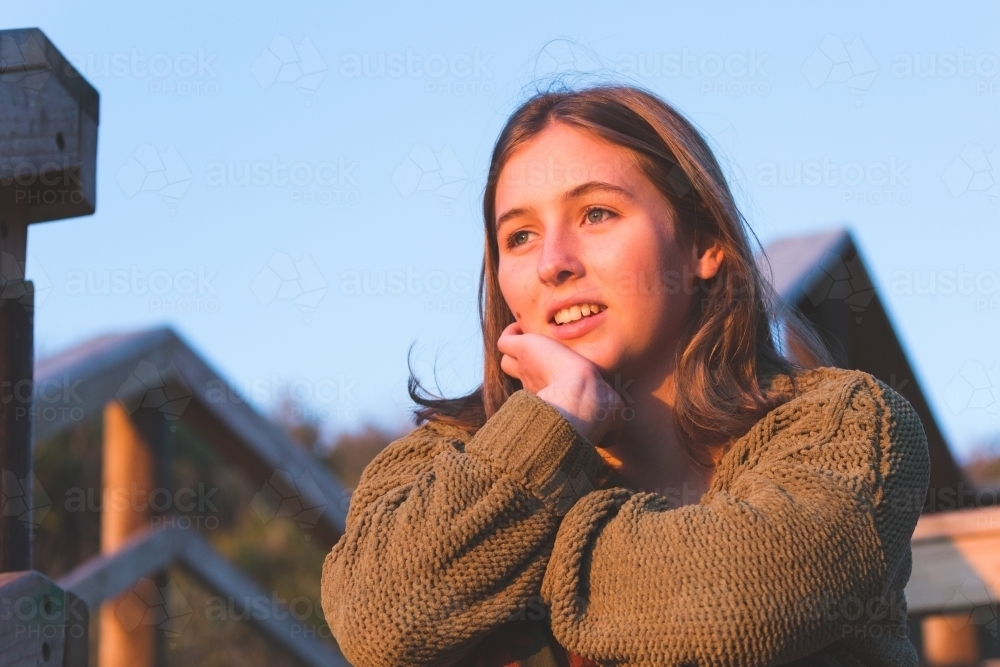 girl outdoors resting chin on hand with blue sky and timber railing behind - Australian Stock Image