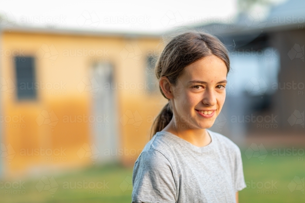 girl outside in yard with rustic building blurred in background - Australian Stock Image