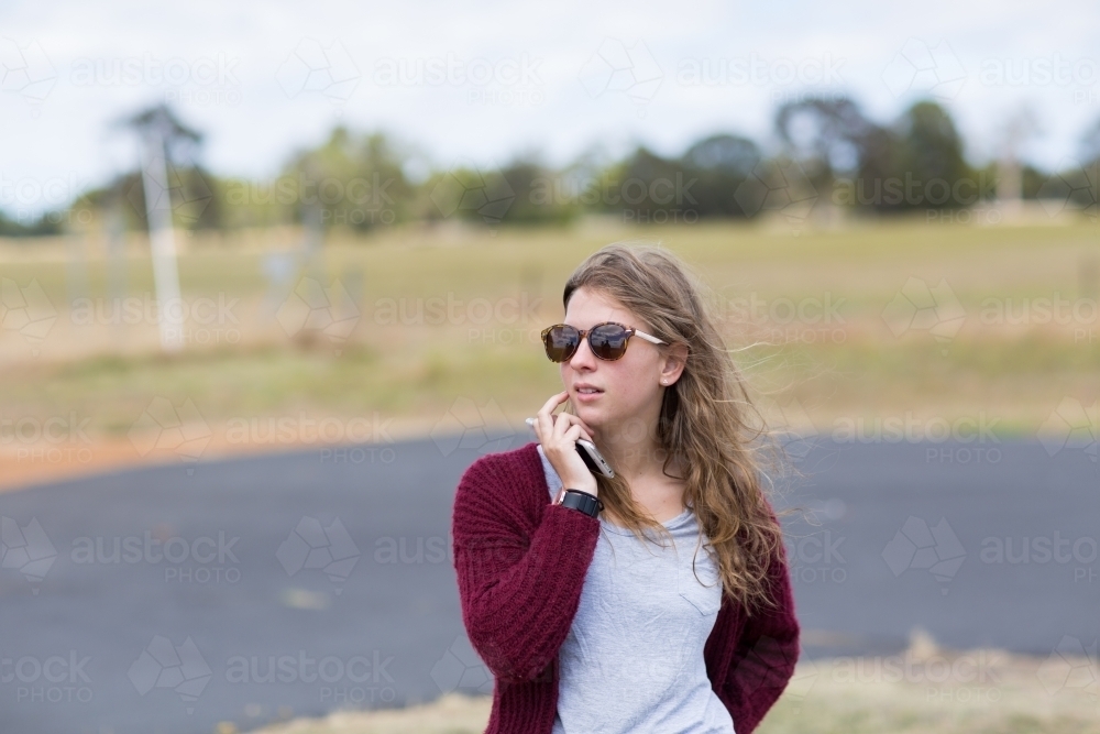 Girl outside wearing sunnies holding mobile phone - Australian Stock Image