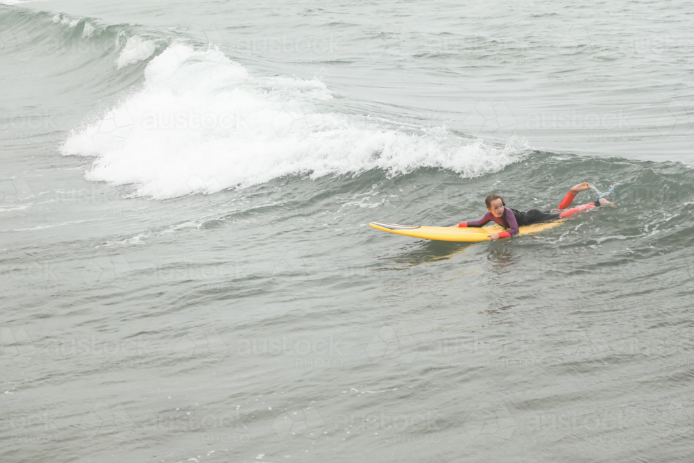 Girl paddling into wave on surf board at the beach - Australian Stock Image