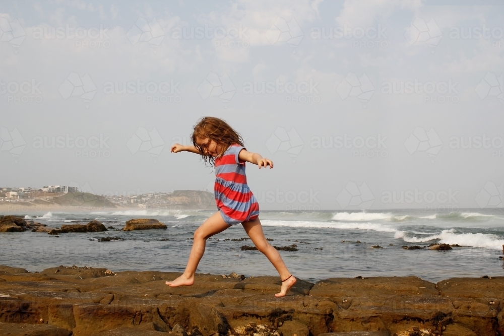 Girl playing in the beach running on rocks at the seashore - Australian Stock Image