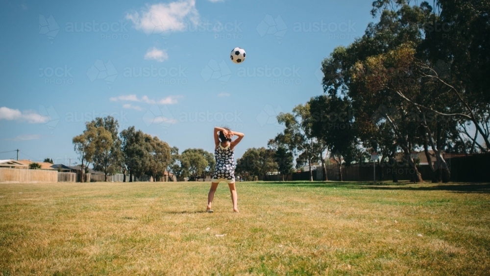 Girl playing soccer in the park with the ball in the air - Australian Stock Image