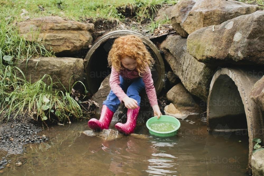 Girl playing with a bucket in the drain - Australian Stock Image