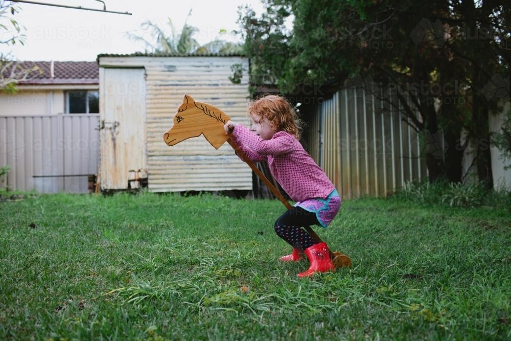 Girl playing with a wooden hobby horse in a backyard - Australian Stock Image