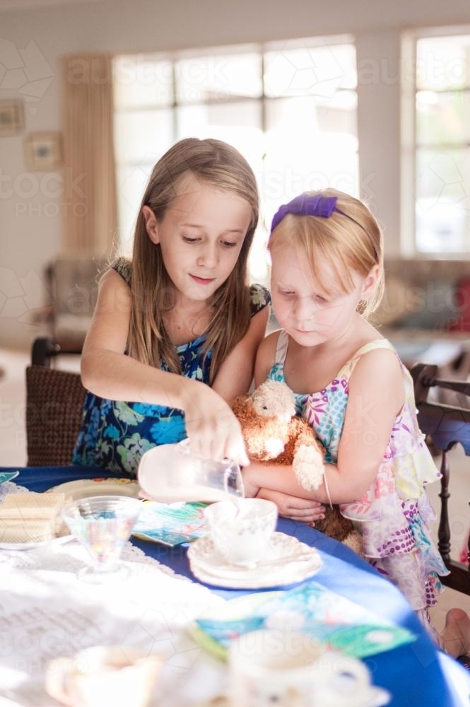 Girl pouring milk into a tea cup at an afternoon tea party for friend - Australian Stock Image