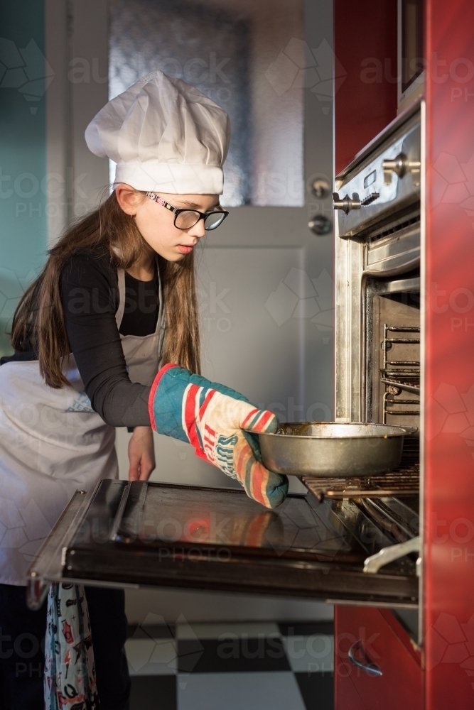 Girl putting cake into oven - Australian Stock Image
