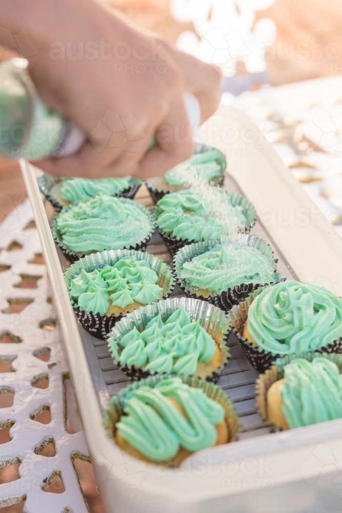 girl putting sugar sprinkles on her birthday cupcakes for school - Australian Stock Image