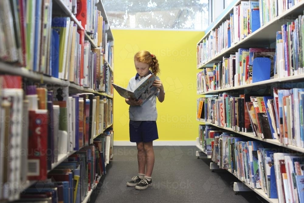 Girl reading a book in a library - Australian Stock Image