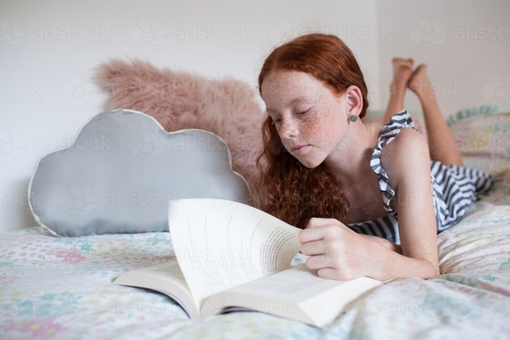 Girl reading a book on a bed - Australian Stock Image